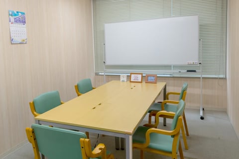 木目調の机に淡いグリーンのひじ掛け付き椅子が5脚あります。