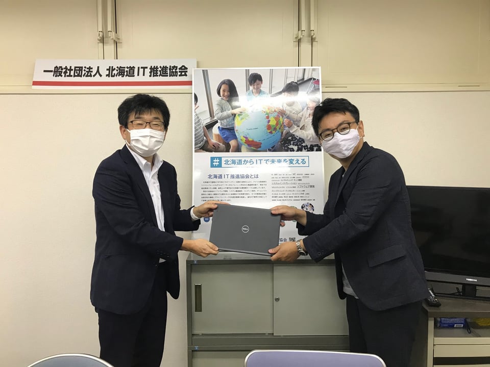 写真：当法人代表の加納が北海道IP推進協会さまからChromebookを受け取っている